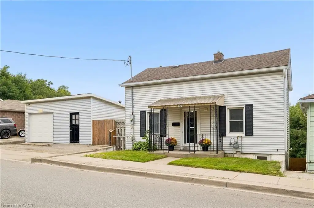 White siding exterior with a pitched roof, front porch with metal railing, and a detached garage with a roll-up door