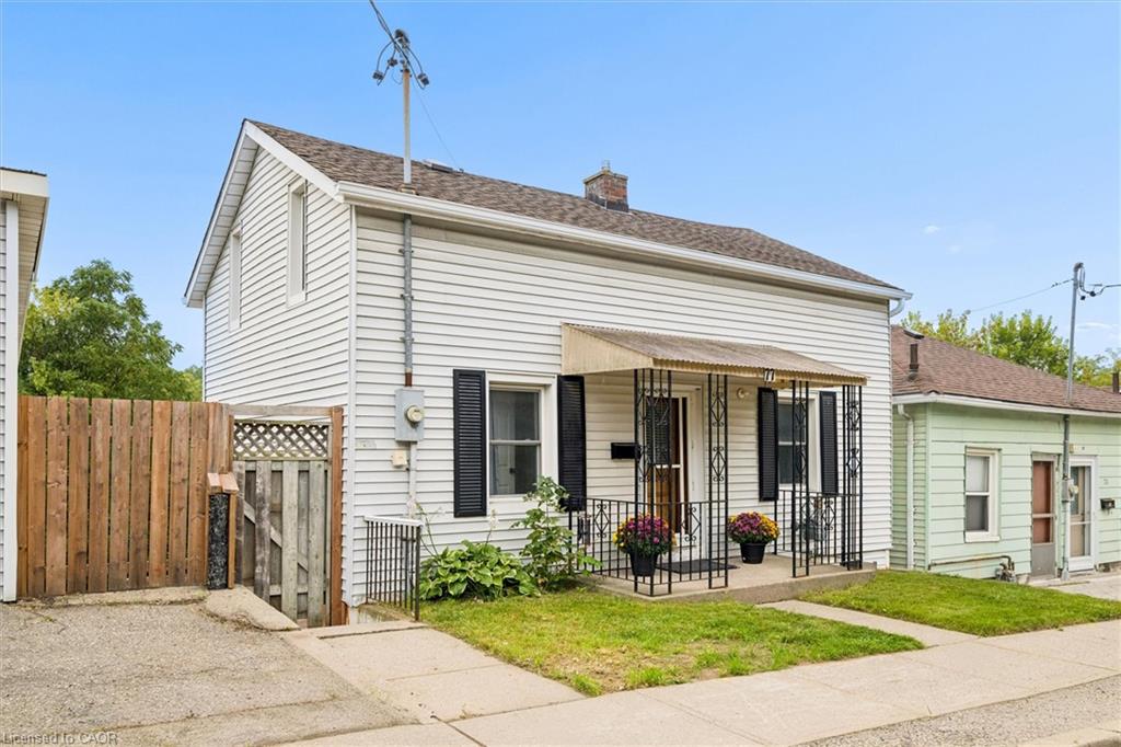 White siding exterior with a pitched roof, front porch with ornate metal railing, and black window shutters
