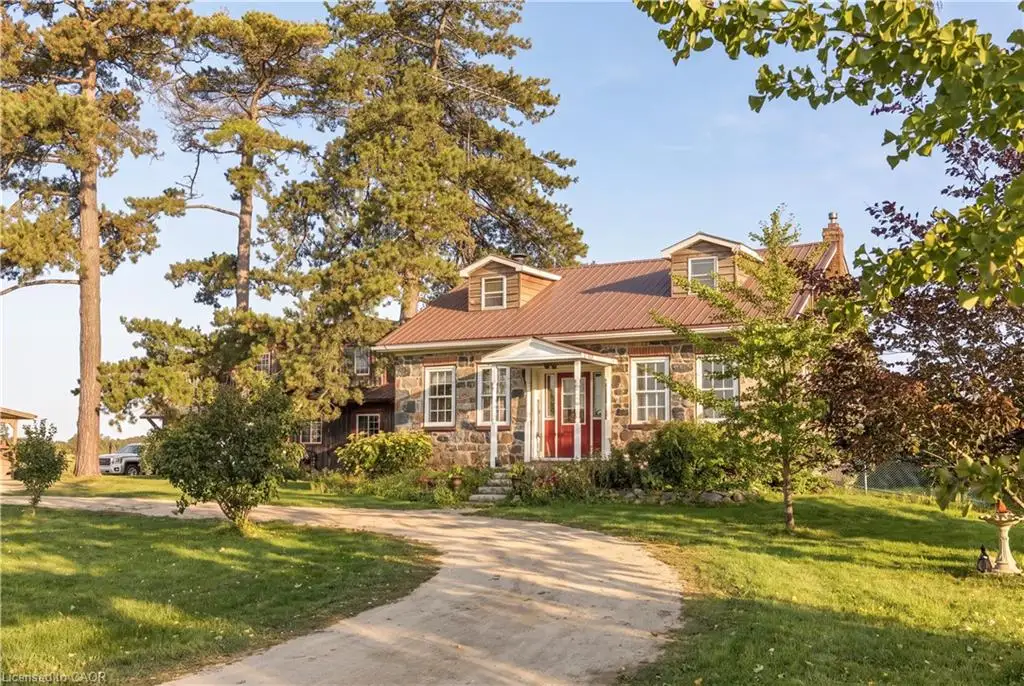 Stone facade residence featuring a metal roof, dormer windows, a covered front porch, and mature trees surrounding the property