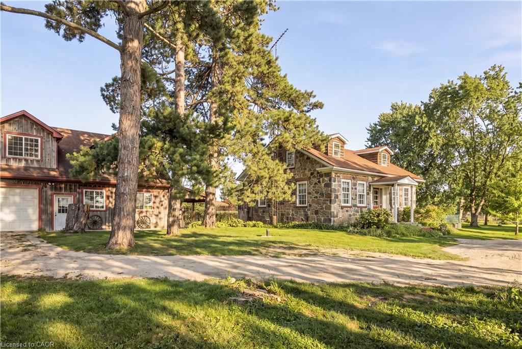 Stone exterior residence with a covered front porch, dormer windows, and a detached two-story structure featuring a garage door and siding