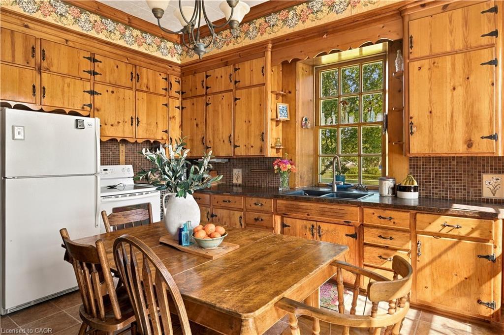 Kitchen featuring wood cabinetry, dark countertops, a mosaic tile backsplash, and a double basin sink with a window above