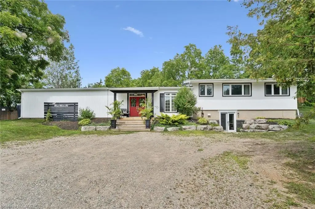 White exterior siding with black trim windows, red entry door, covered entry, and gravel driveway