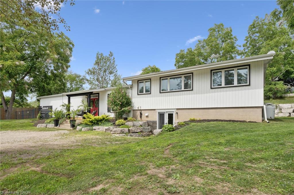 White exterior siding with black-trimmed windows, a prominent red front door, and a stone retaining wall