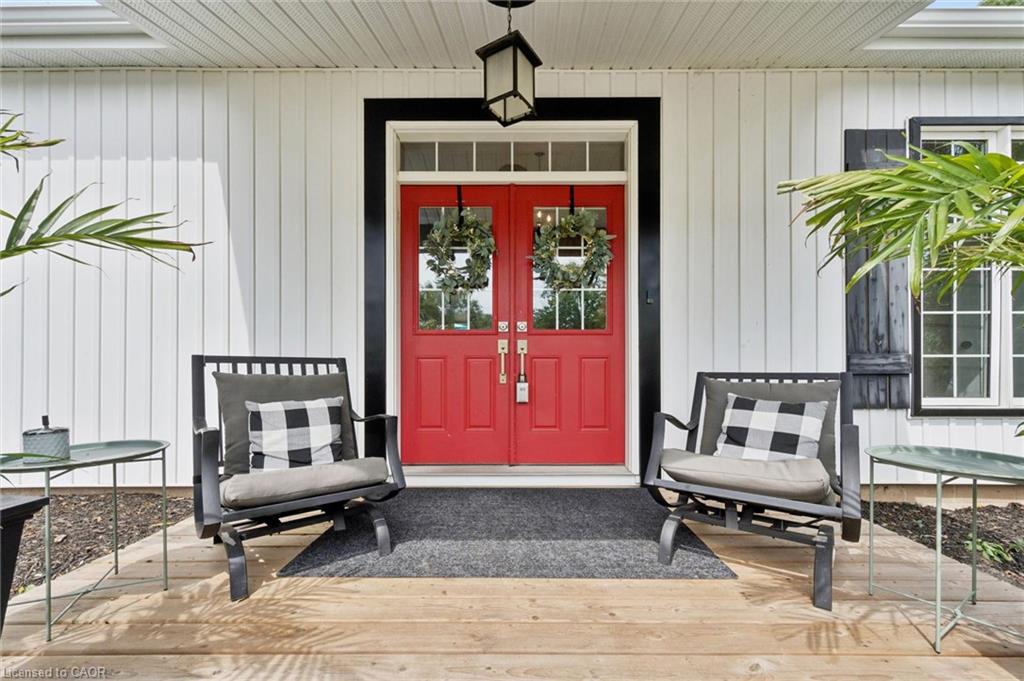 Board and batten siding, red double entry doors, black trim details, white window frames, and natural wood-finish porch flooring