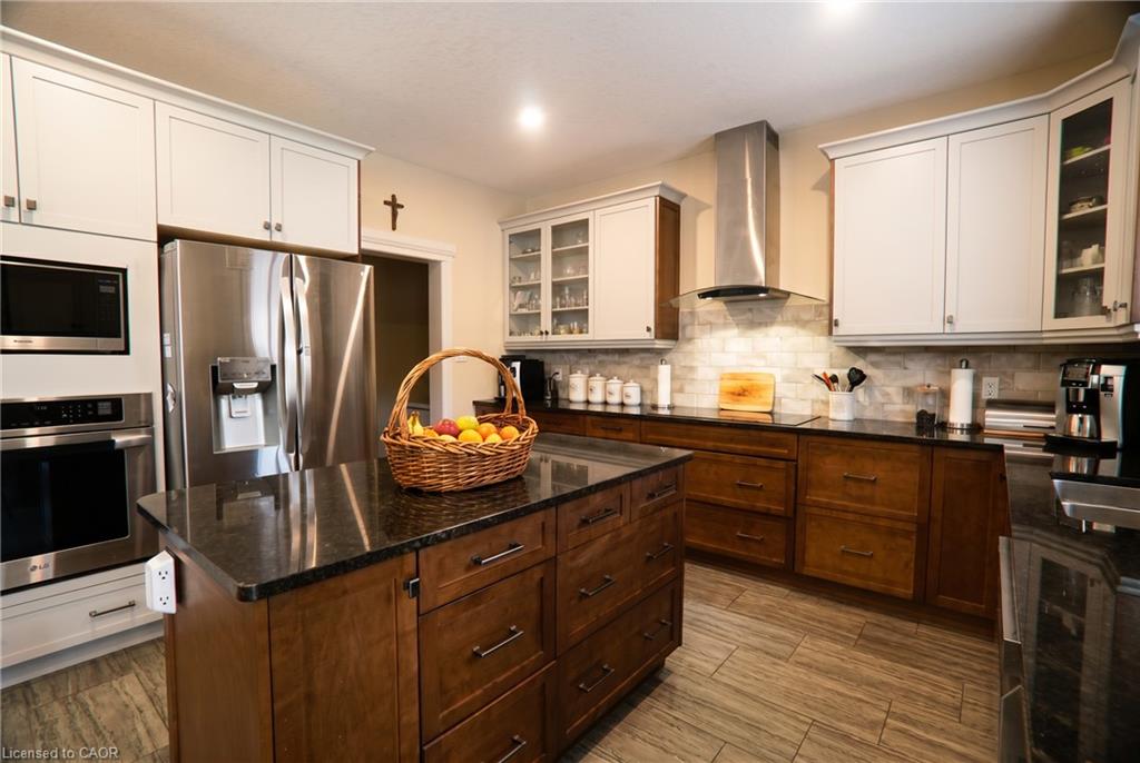 Kitchen featuring a central island with dark stone countertop, built-in stainless steel appliances, two-tone cabinetry, and a subway tile backsplash