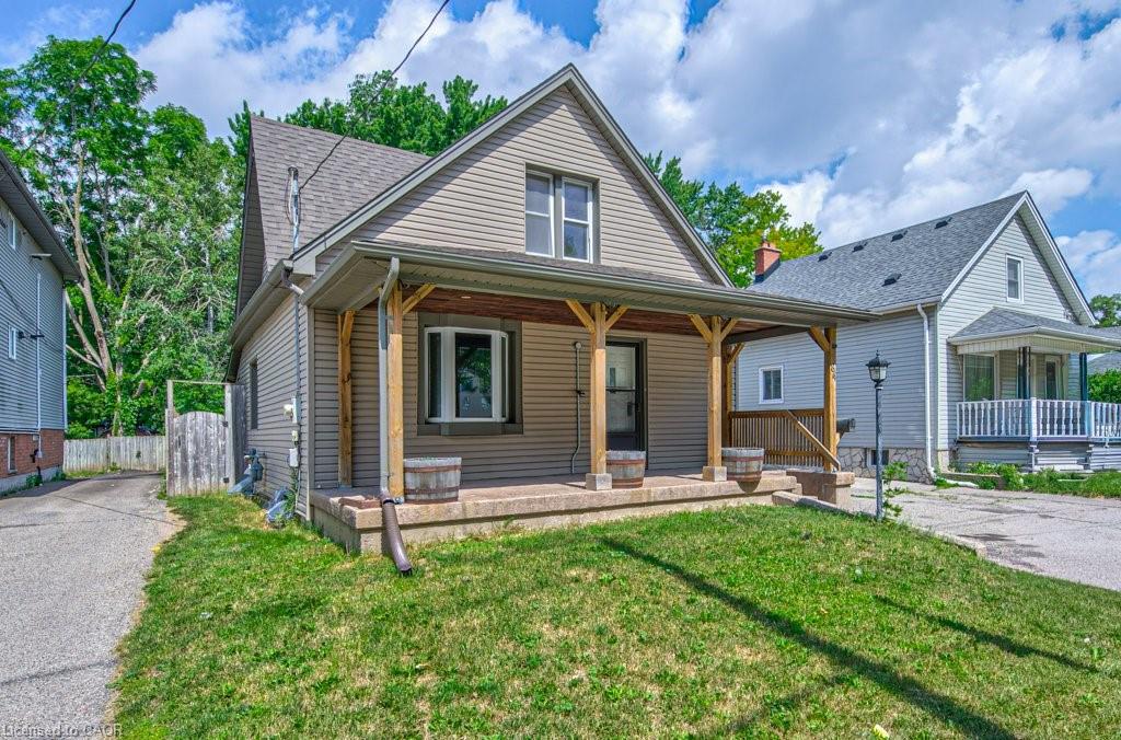 Beige siding exterior with a dark-shingled gable roof, featuring a covered front porch with exposed wood beams and a concrete foundation