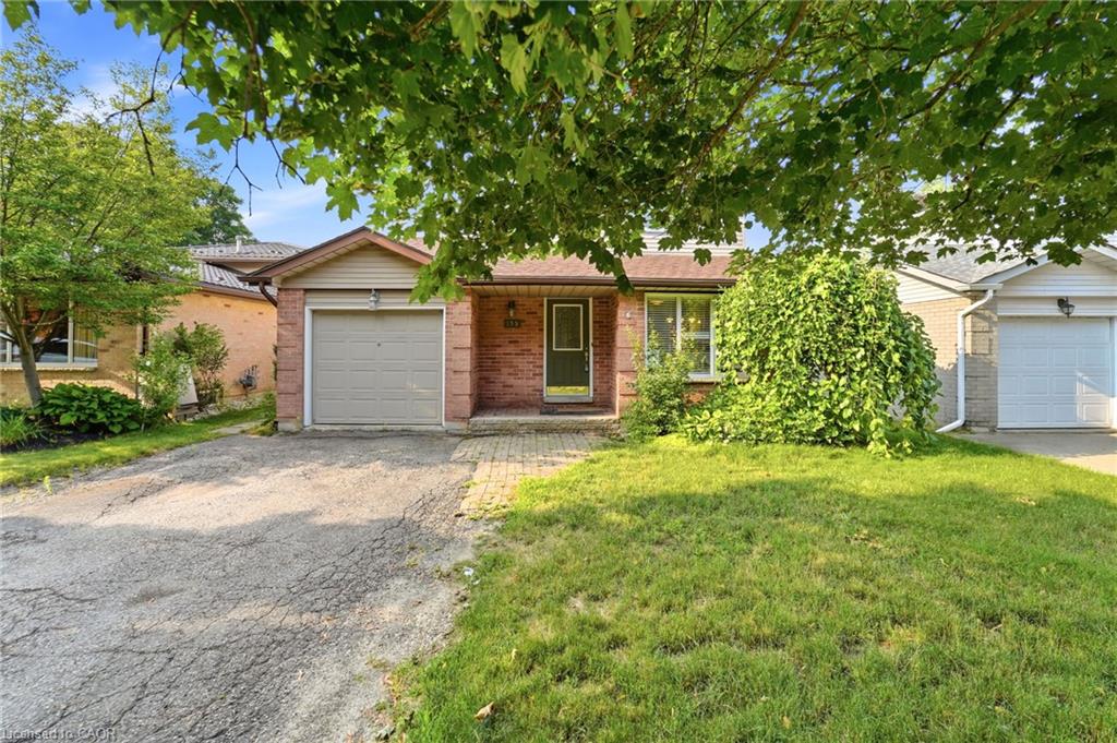 Brick exterior with an attached garage, paved driveway, and mature front landscaping
