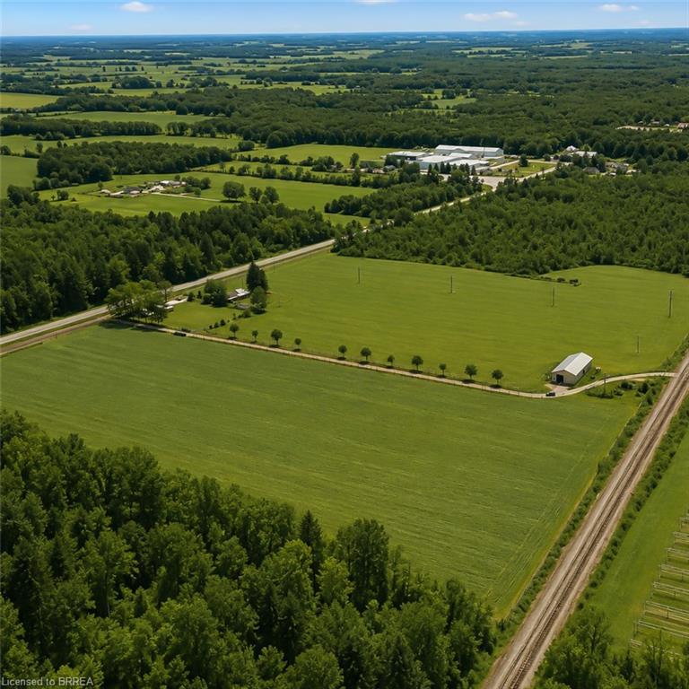 Expansive green fields bordered by mature tree lines, featuring a highway, railroad tracks, and distant structures