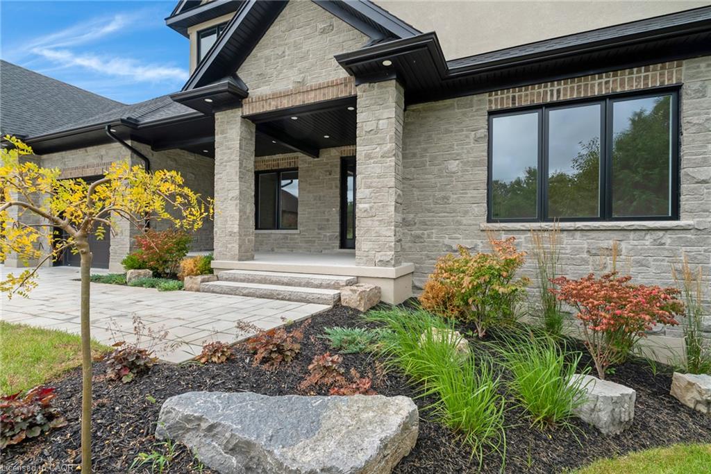Stone veneer exterior with dark trim accents, covered entry, multiple windows, and extensive landscaping with decorative rock features