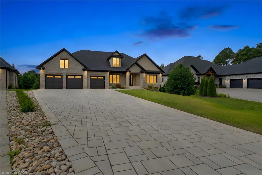 Exterior featuring a paver driveway, stone facade, multiple garage doors, and a dark roof