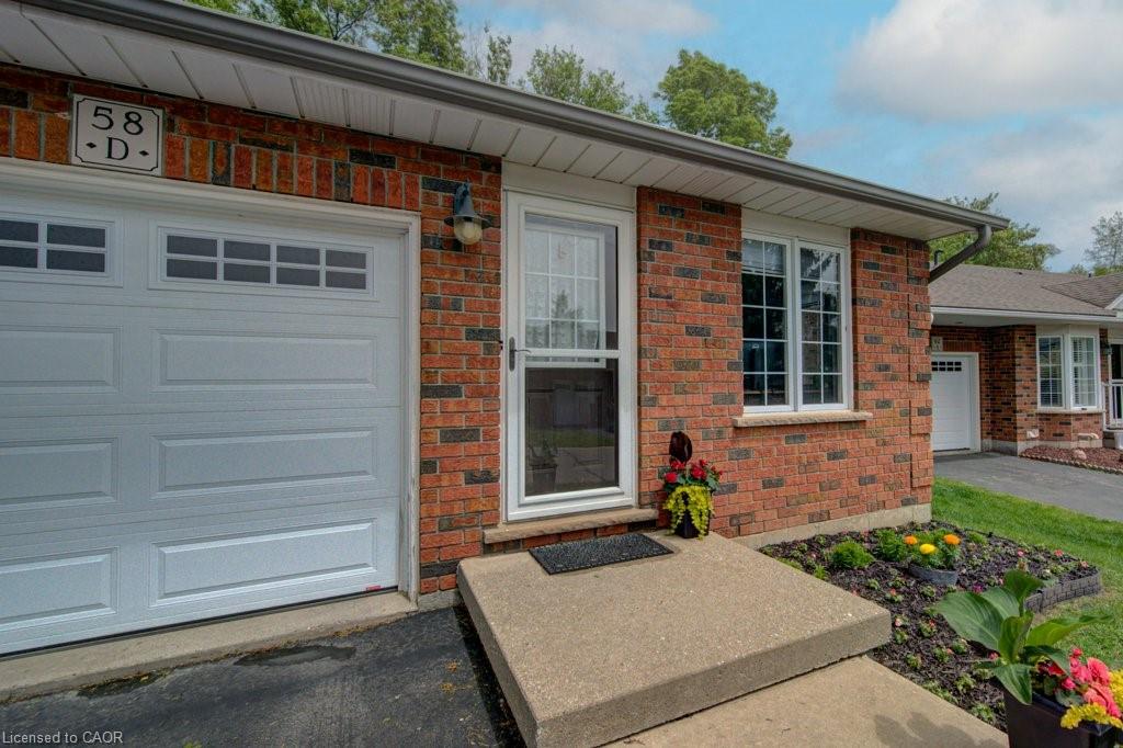 Red brick exterior featuring a white garage door with upper window inserts, white-framed windows, a concrete walkway, and a landscaped garden bed