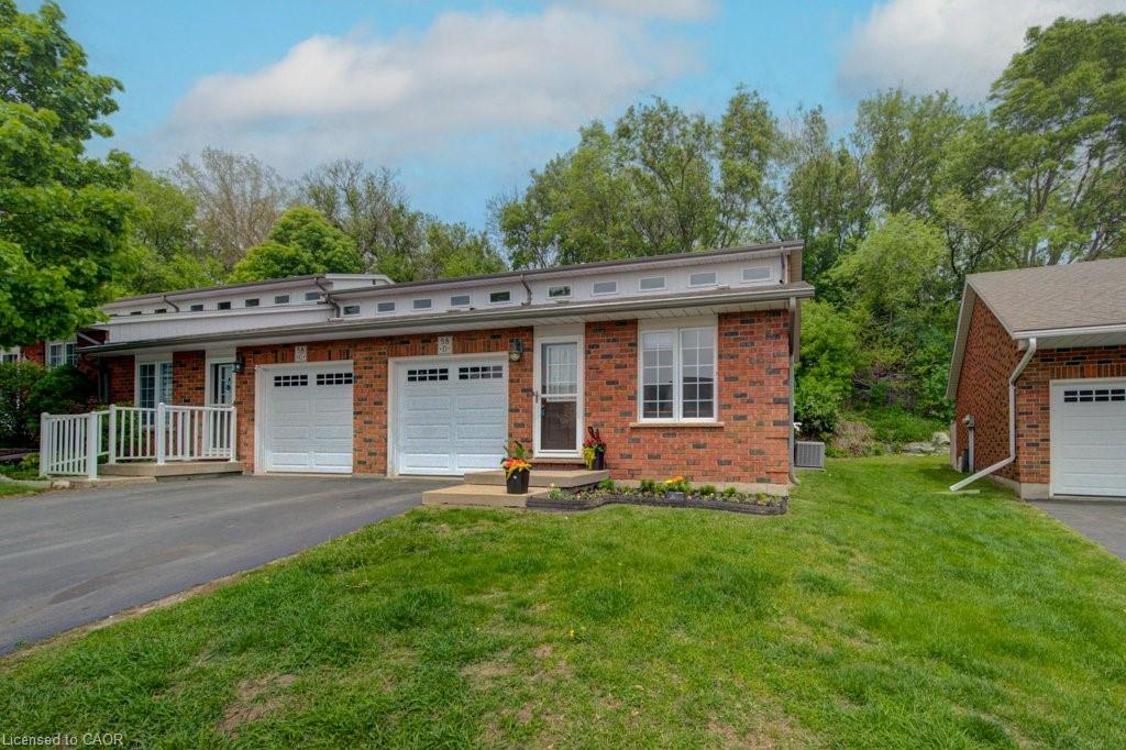Brick facade townhouse with two white garage doors, white window frames, a front entry with a small garden bed, and a paved driveway