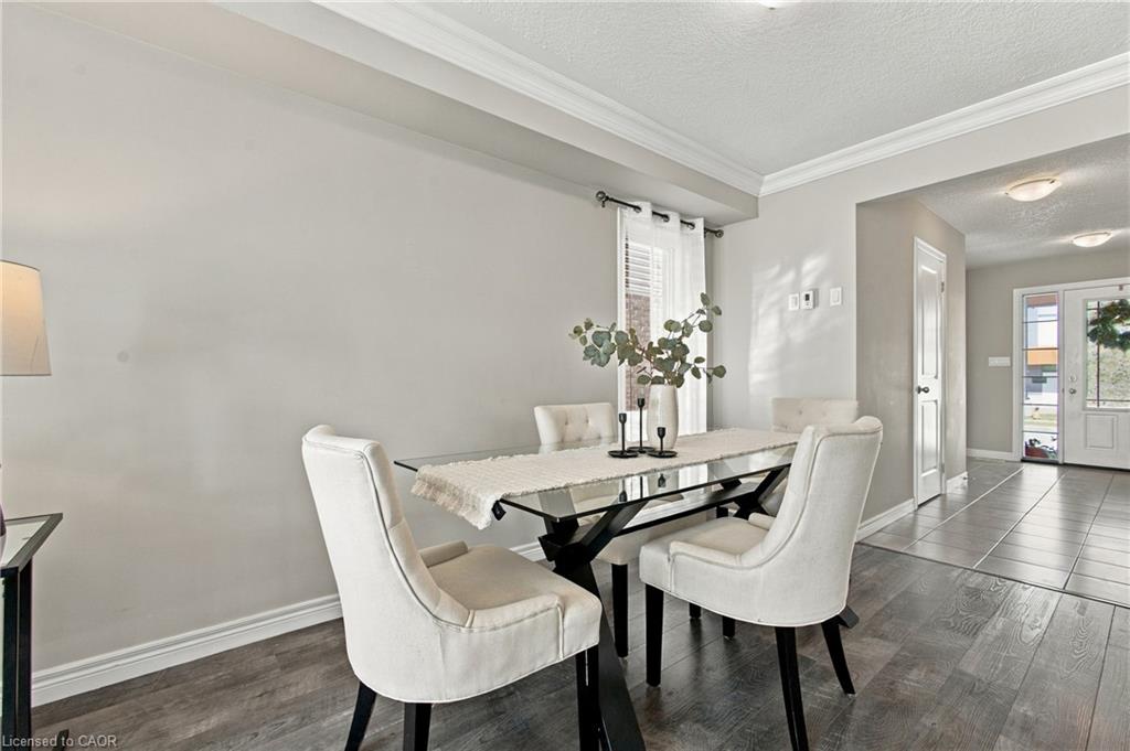 Crown molding accents this dining space, featuring a window with blinds, wood-finish flooring, and a tiled entryway