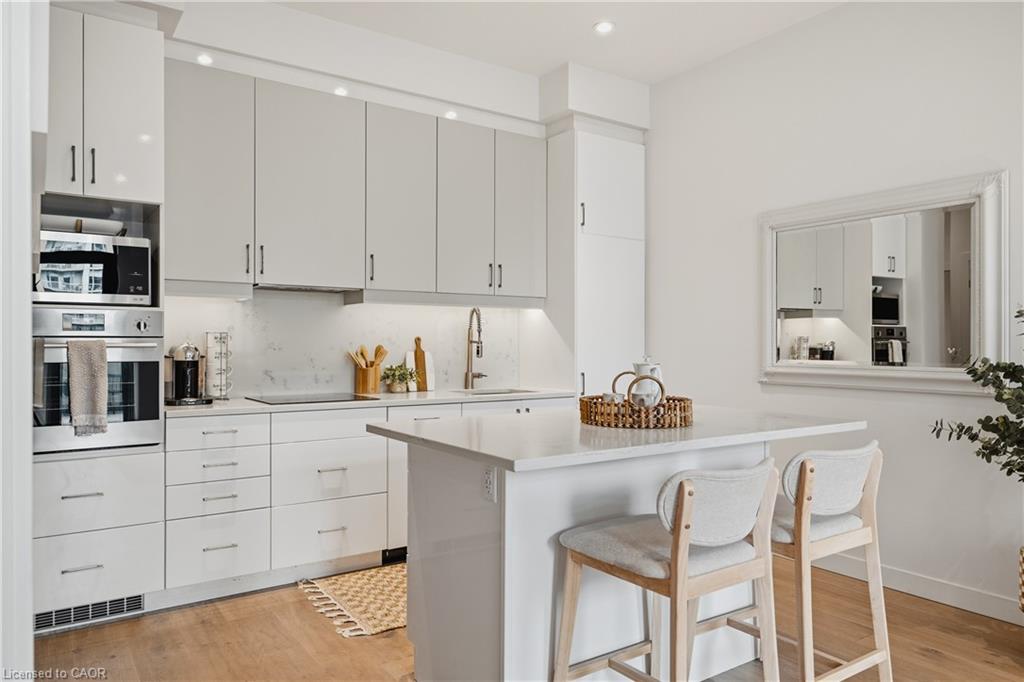 Contemporary kitchen featuring sleek white cabinetry, integrated stainless steel appliances, a generous island with a solid surface countertop, recessed lighting, and wood-finish flooring