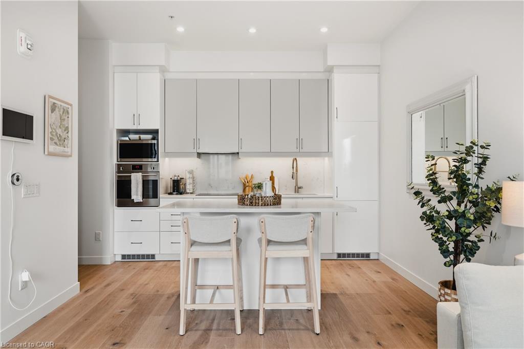 Modern kitchen featuring a central island with seating, stainless steel built-in appliances, two-tone cabinetry, and wood-finish flooring