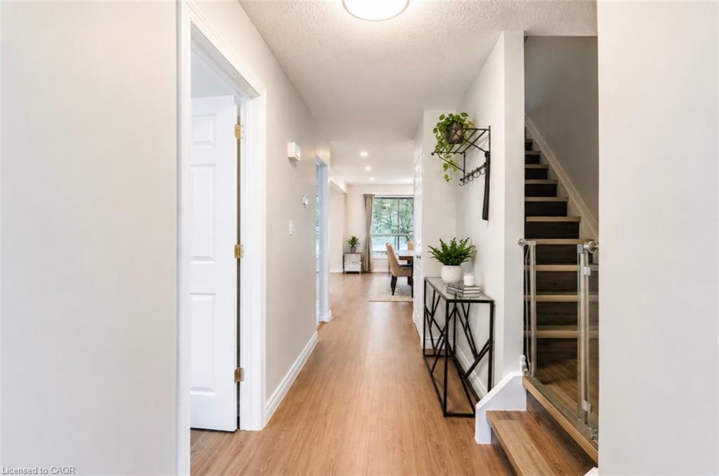 Bright hallway featuring wood-finish flooring, a contemporary staircase with glass railing, and a console table
