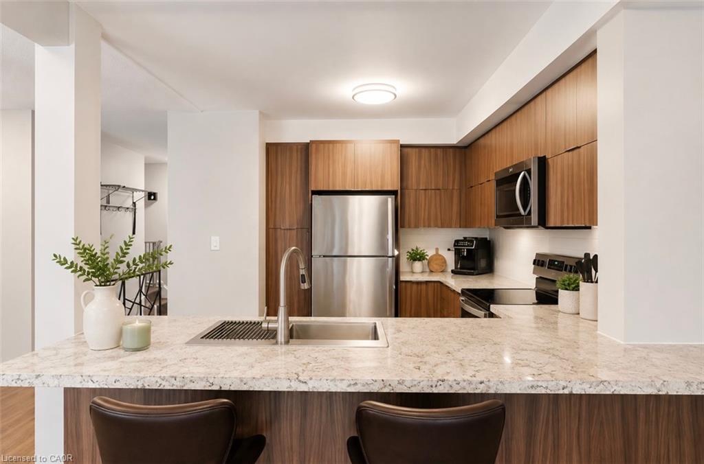 Kitchen featuring a spacious island with stone countertops, an undermount sink with a gooseneck faucet, stainless steel appliances, and wood-finish cabinetry