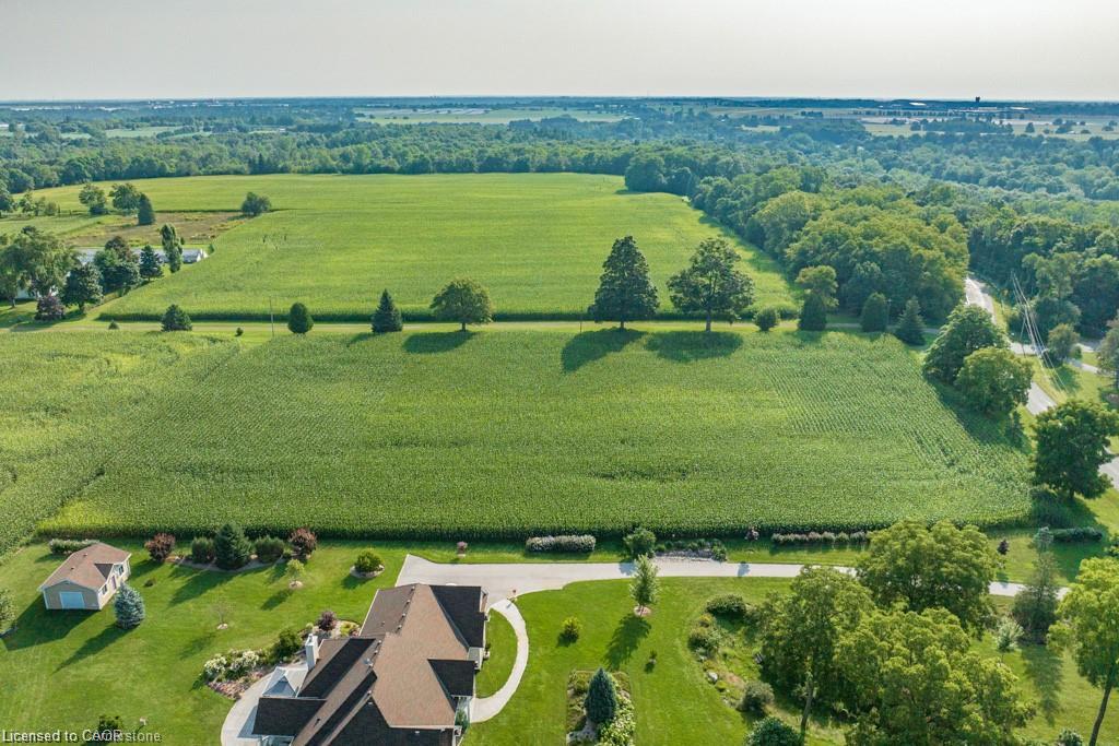 Expansive rural property featuring a large residence with a multi-gabled roof, a detached auxiliary building, manicured lawns, mature trees, and agricultural fields