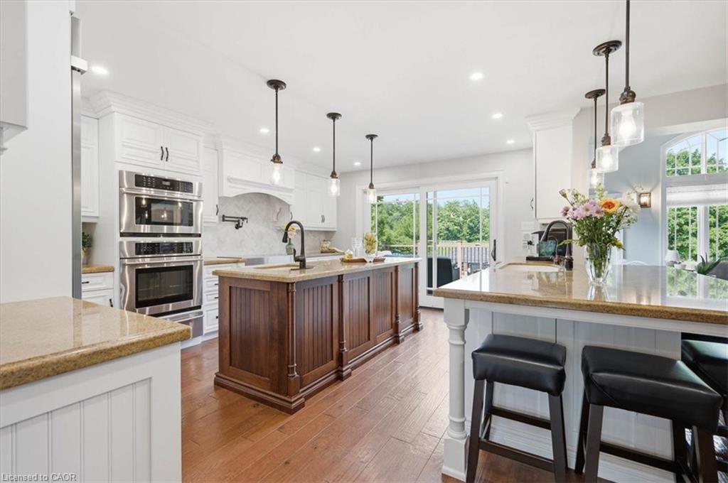 Spacious kitchen featuring two-toned cabinetry, hand scraped engineered hardwood, a double island with seating, stainless steel double wall oven and microwave, and a sliding glass door leading to exterior space.