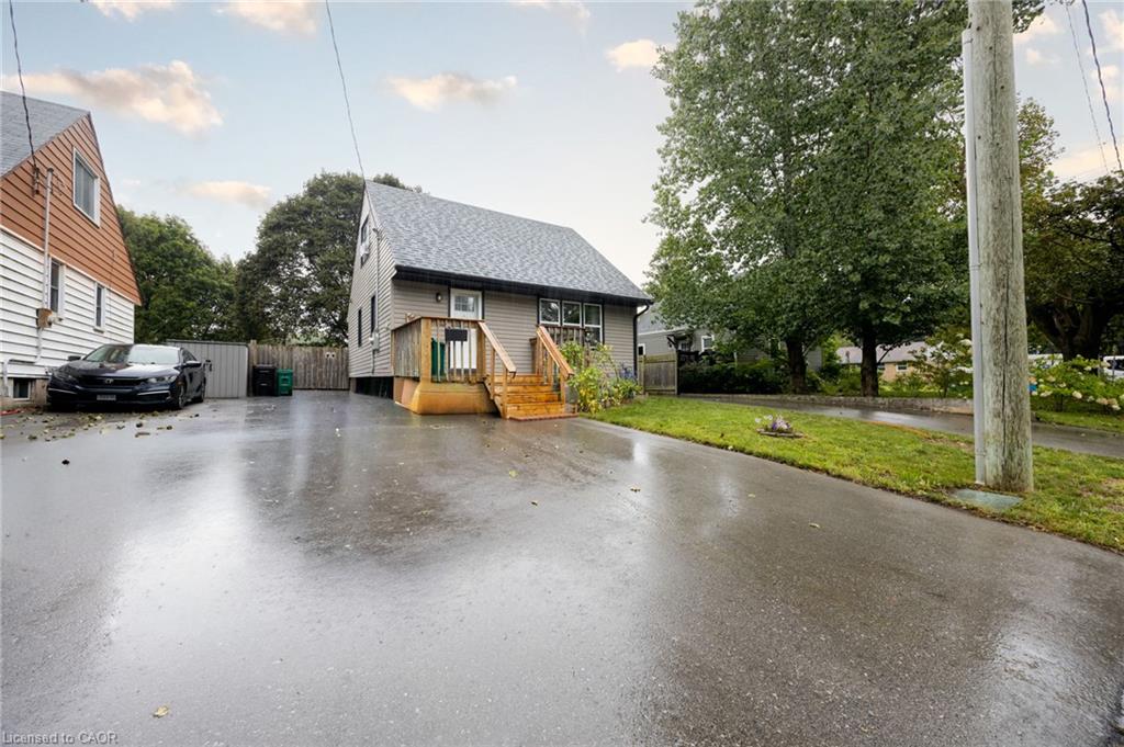 Asphalt driveway with a fenced property line, wood siding, and mature trees
