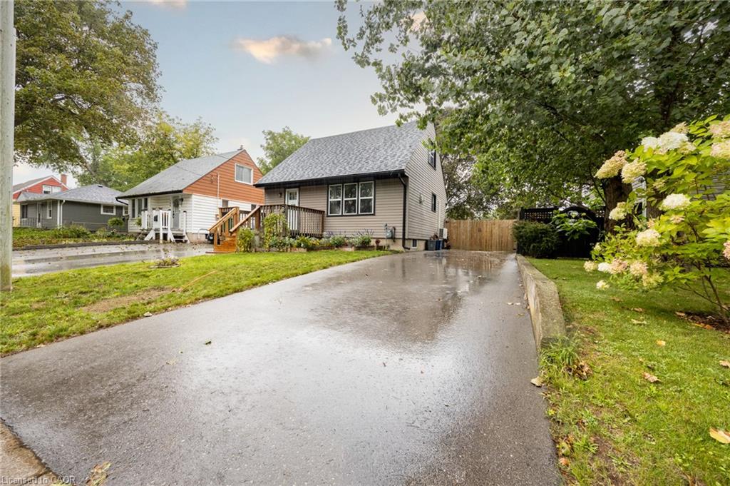 Paved driveway, manicured lawn, established landscaping, and wood privacy fence
