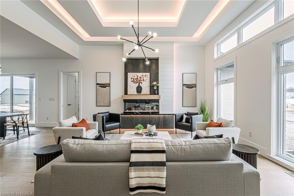 Spacious living area featuring a tray ceiling with integrated lighting, a striking linear chandelier, wood-finish flooring, and large windows