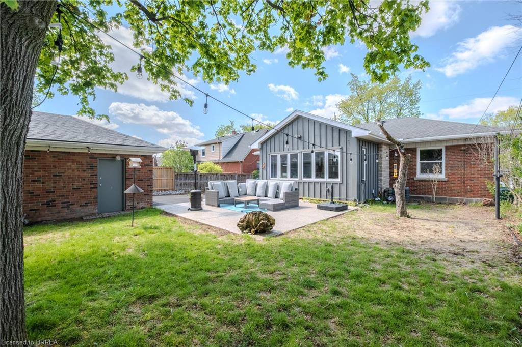 Expansive backyard featuring a concrete patio, a sunroom with large windows, and a detached brick structure