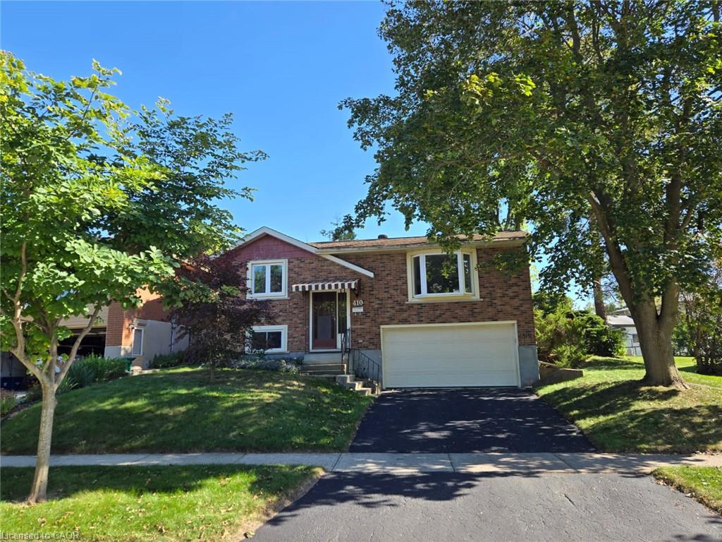 Brick exterior, single garage, paved driveway, mature trees, and a front yard with established landscaping