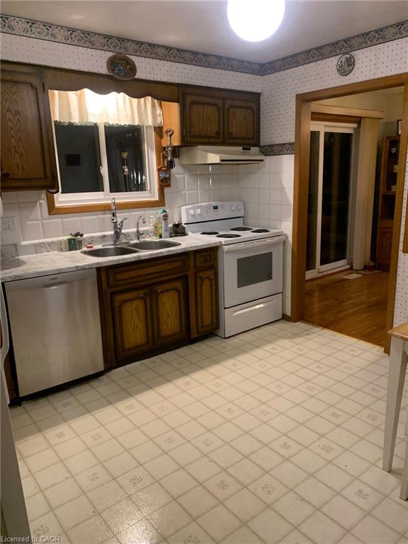 Wood-finish cabinetry, white tile backsplash, a stainless steel dishwasher, a white range, and a dual basin sink