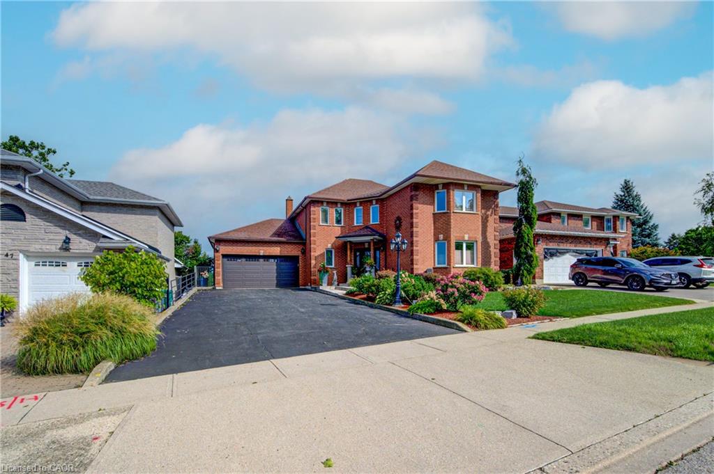 Brick exterior with a brown shingle roof, paved driveway, two-car garage, and established landscaping