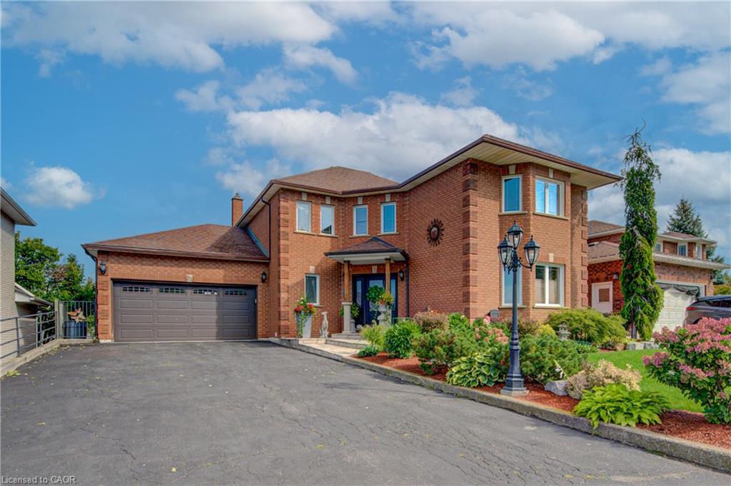 Brick-clad exterior with multiple windows, an attached two-car garage, a paved driveway, and manicured landscaping