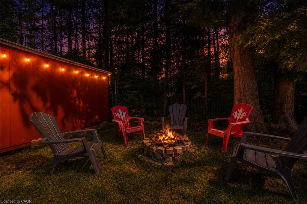Expansive grassy yard featuring a stone fire pit, string lighting, and mature trees