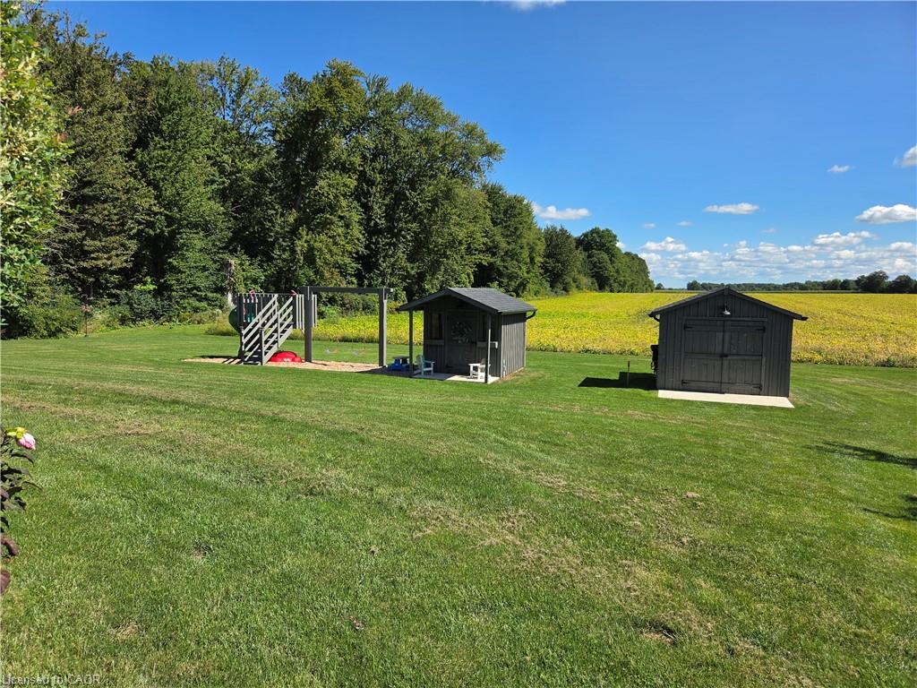 Expansive lawn featuring two storage sheds, a play structure, and mature trees bordering the property