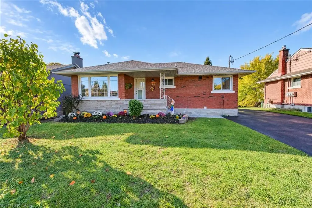 Single-story red brick exterior featuring a covered front porch, stone masonry detailing, a wide multi-pane front window, and an asphalt driveway