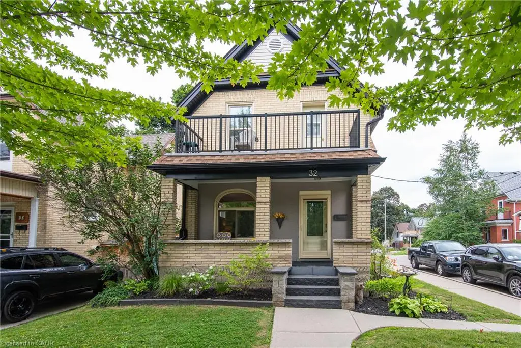 Brick exterior featuring a covered front porch, an upper-level balcony with metal railings, a manicured front lawn, and established landscaping